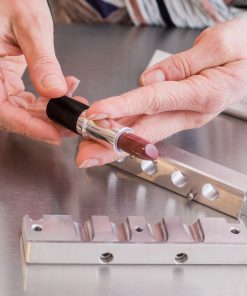 a person holding a tube with a red custom lipstick that has just been removed from the lipstick making mold