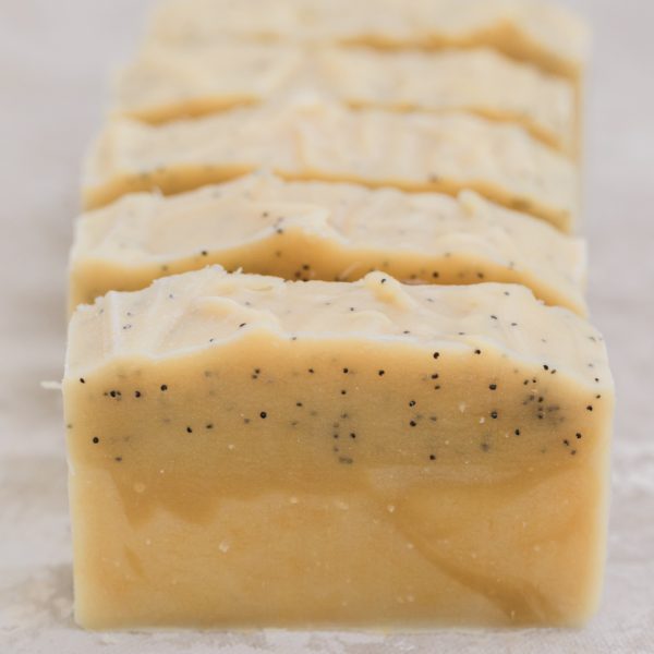 a group of five handmade soaps lemon poppyseed a yellow soap with swirls and poppyseeds