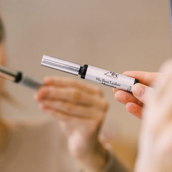 woman holding tube of clean mascara in a mirror deciding it is safe for sensitive eyes
