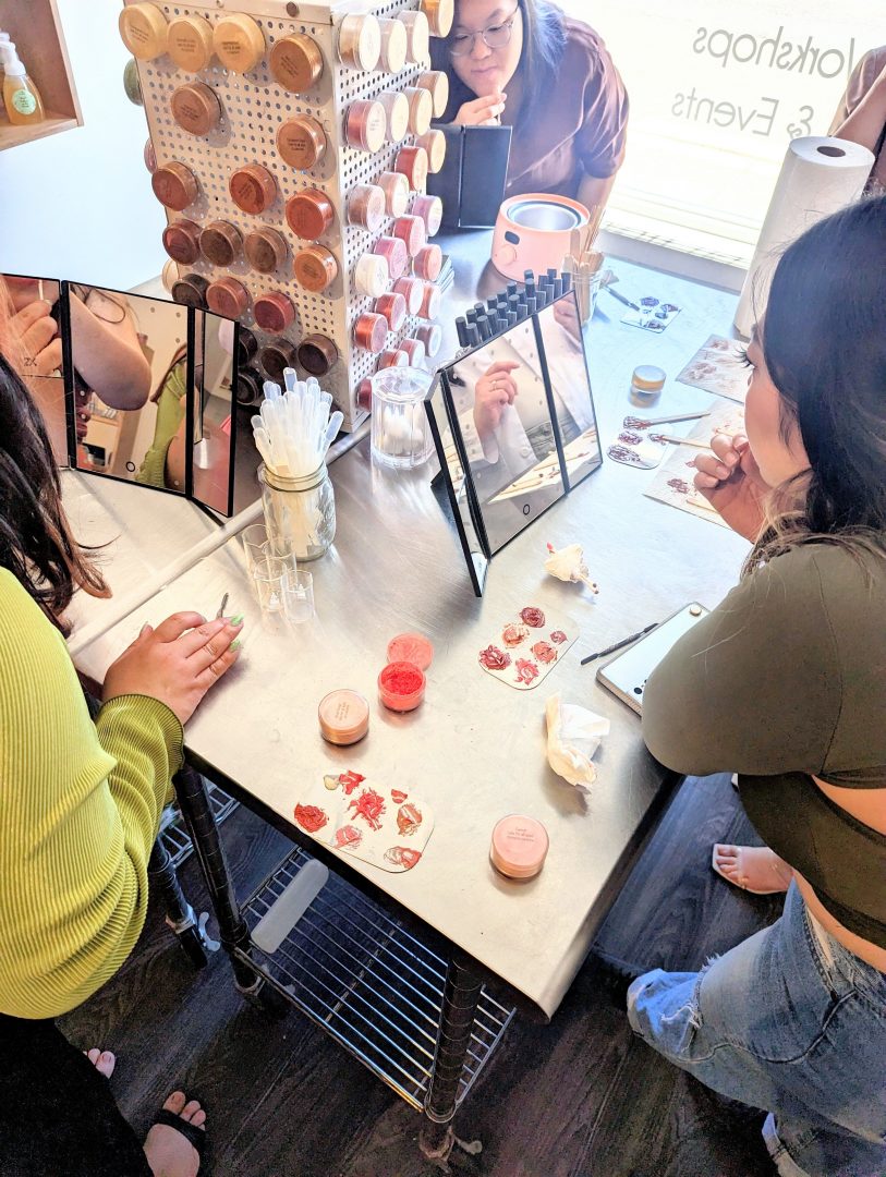 A group of friends at a bachelorette party smiling and making custom lip gloss at Mix Cosmetiques in Superior, WI. Each person is mixing plant-based ingredients to create personalized beauty products. The peaceful, creative studio atmosphere offers a unique experience where guests can bring their own food and drinks for a fun and exclusive celebration.