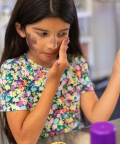 a teen girl looking in the mirror to try no more masquerade an acne-fighting hydrating detoxing honey clay facial mask