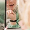 someone applying custom, hydrating lip gloss in front of a mirror to try plumping hyaluronic acid lip gloss formula made with plant-based ingredients